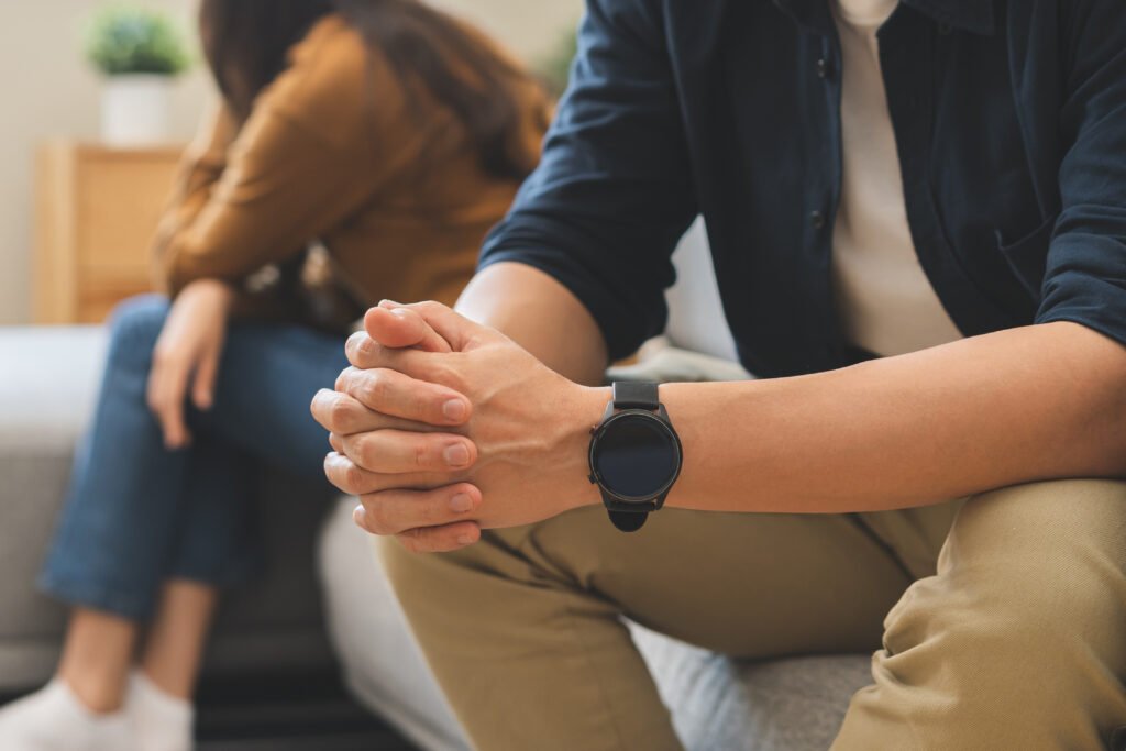 Un couple en conflit assis à distance sur un canapé, illustrant une situation nécessitant une ordonnance de protection.